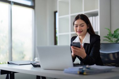 Ofiste bilgisayarını ve telefonunu kullanan genç ve güzel bir iş kadını..