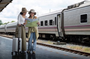 Seyahat konsepti. Kız arkadaşının şapka taktığı harita çanta ve bavulu var. Tren istasyonunda bekleyen kadın yolcu..