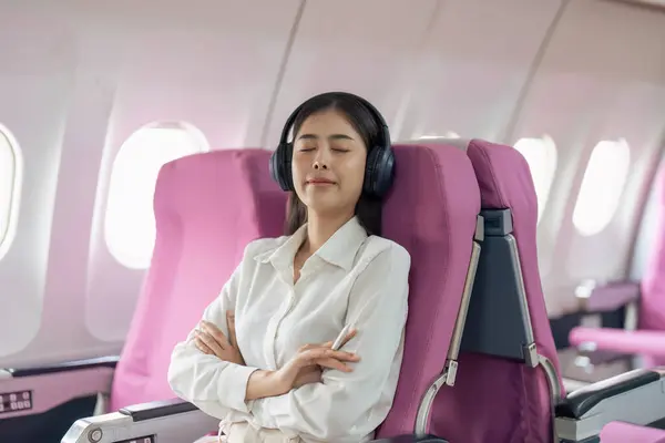 在机舱里的亚洲女人 一边在飞机上听音乐 一边戴着耳机休息 — 图库照片