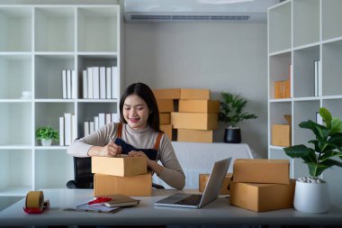 İnternetten ecommerce alışverişinde çalışan genç bir kadın. Genç bir kadın müşteriye teslim etmek için bir paket ürün satar. Çevrimiçi satış, ekommerce. Ürün çevrimiçi satılıyor.