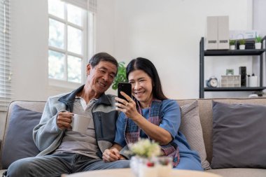 Akıllı telefon kullanan mutlu Asyalı çift evdeki internet sitesinde ekommerce alışverişi yapıyor..