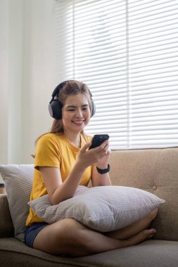 Genç Asyalı bir kadın müzik dinlemek ya da evde sohbet etmek için cep telefonu ve kulaklık kullanıyor..