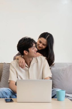 Asyalı genç çift evdeki kanepede otururken dizüstü bilgisayar kullanıyor..