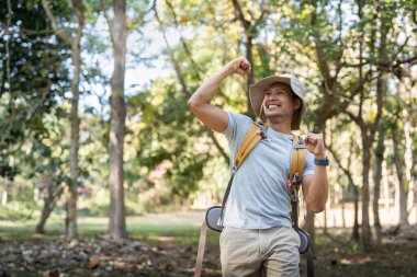 Asyalı genç adam sırt çantasıyla ağaçların arasında yürüyor, genç adam ormanda tek başına eğleniyor. Kamp, yürüyüş, seyahat, macera arayışı.