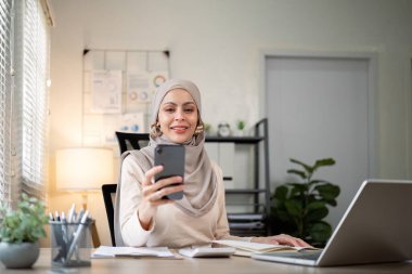 İşadamı Müslüman bayan girişimci ofiste dizüstü bilgisayarla çalışıyor, cep telefonuyla iş görüşmesi yapıyor..
