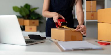 Kadınlar paket kutuları eklemek için koli bandı kullanırlar ve evde paketleme, nakliyat, çevrimiçi satış İnternet pazarlama ekommerce konsepti başlangıç iş fikri için ürünleri hazırlarlar..