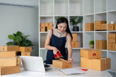 Asyalı kadın, paketleme, nakliye, çevrimiçi satış İnternet pazarlama ekommerce konsepti başlangıç iş fikri için paket kutuları eklemek için koli bandı kullanıyor.