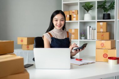 Genç iş kadını Asyalı dükkanında online ecommerce alışverişi yapıyor. Genç bir kadın müşteriye teslim etmek için bir paket ürün satar. Online satış.