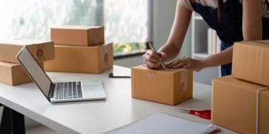 İnternetteki bir kadın kutunun üzerindeki müşteri adresini ve paket bilgilerini kontrol eder. Çevrimiçi alışveriş kavramı.