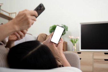 Yetişkin kız elinde beyaz ekran maketli akıllı telefon tutuyor ve internet kullanıyor. Büyük anne ve yetişkin kızı evde..