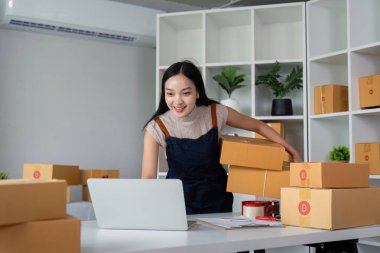 Serbest çalışan Asyalı kadın girişimcisi online olarak sipariş almak ve gözden geçirmek için dizüstü bilgisayar ve kutu kullanarak müşterilere, çevrimiçi iş fikirlerine satış yapmaya hazırlanıyor..