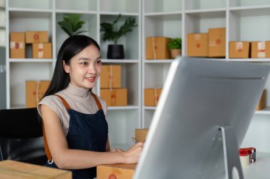 İnternetteki Asyalı kadın kutunun üstündeki müşteri adresini ve paket bilgilerini kontrol et. Çevrimiçi alışveriş kavramı.