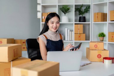 Genç iş kadını Asyalı dükkanında online ecommerce alışverişi yapıyor. Genç bir kadın müşteriye teslim etmek için bir paket ürün satar. Online satış.