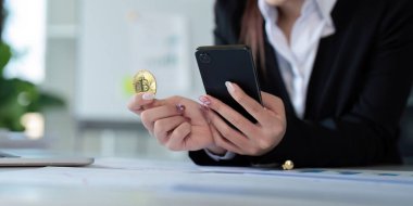 Altın bir Bitcoin tutan iş kadını. Grafik çizelgesi ile cep telefonu kullanımı, borsa ticareti, merkez ofise Bitcoin kripto para yatırımı. Yatırım ve teknoloji kavramı.