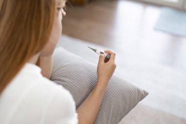 Evde termometre tutan hasta genç bir kadın. Hastalık, sağlık ve kişisel bakım kavramı.