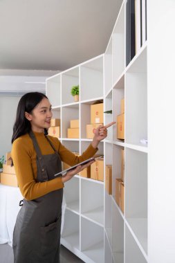 İşletme sahibi, ev ofisindeki stokları ve envanterleri kontrol ediyor. Küçük işletme girişimcisi sevkiyat için paketler düzenliyor ve envanter takibi için bir tablet kullanıyor.