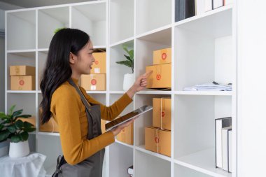 Ticaret sektörü sahibi, envanteri düzenliyor ve ev ofisindeki stokları kontrol ediyor. Paketleri yöneten ve envanter takibi için bir tablet kullanan küçük işletme girişimcisi.