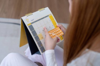 Doğum kontrol hapı tutan ve takvimi kontrol eden bir kadın. Doğum kontrolü ve aile planlaması kavramı.