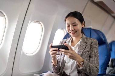 Uçakta akıllı telefon kullanan gülümseyen bir iş kadını. Uçuş iletişimi ve iş seyahati kavramı.