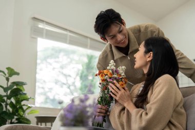 Evde bir buketi paylaşan genç bir çift. Sevgi, şefkat ve birliktelik kavramı.