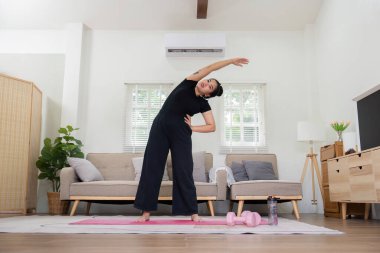 Oturma odasındaki yoga minderinde yan esneme hareketi yapan bir kadın, ev çalışmasının ve esnekliğinin altını çiziyor.