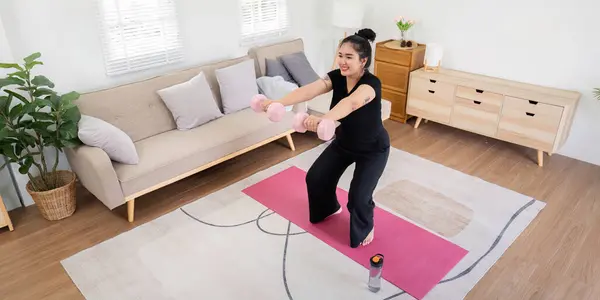 stock image Overweight woman exercising with dumbbells in a modern living room, showcasing weight loss journey and healthy lifestyle.
