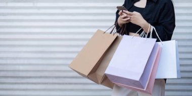Akıllı telefon kullanırken elinde birden fazla alışveriş çantası tutan kadın Kara Cuma alışverişini ve perakende satışını temsil ediyor..