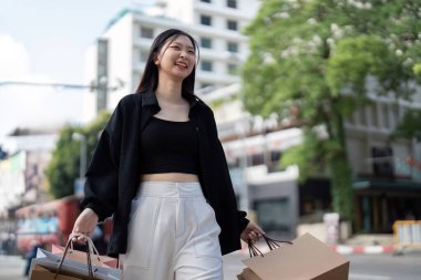 Kara Cuma satışları sırasında şehirde çoklu alışveriş torbaları taşıyan gülümseyen genç bir kadın heyecan ve neşe sergiliyor..