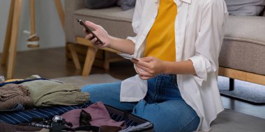 Yaz tatili için bilet ve otel ayırtmak için kredi kartı ve akıllı telefon kullanan bir kadın. Yolculuk için valiz hazırlayan, modern seyahat ve online rezervasyon kavramını temsil eden bir kadın..