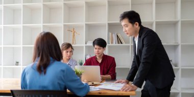 Çeşitli bir iş ekibi, arka planda açık rafların yer aldığı modern ofis ortamında bir tartışma ve analizle meşgul oldu..