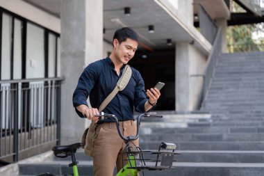 Bisikletli bir iş adamı, akıllı telefon kullanıyor, modern bir şehir ortamında çevre dostu ve sürdürülebilir ulaşımı teşvik ediyor..