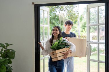 Neşeli bir çift yeni evlerine taşınıyor, kutuları ve bitkileri taşıyorlar, parlak ve modern bir evde yeni bir başlangıç ve başlangıcı simgeliyorlar..