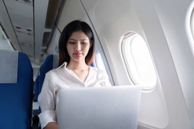 Uçak uçuşu sırasında dizüstü bilgisayarda çalışan profesyonel iş kadını modern şirket seyahatlerini ve uçuş verimliliğini gösteriyor..