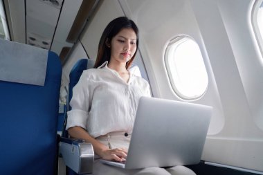 Uçakta seyahat ederken dizüstü bilgisayarda çalışan bir iş kadını modern şirket seyahatleri ve uçuş verimliliği sergiliyor..