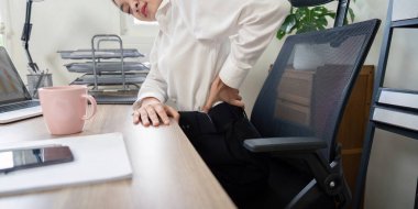 Ofis masasında çalışırken sırt ağrısı çeken bir iş adamı, iş sağlığı ve ergonomik konularını vurguluyor.
