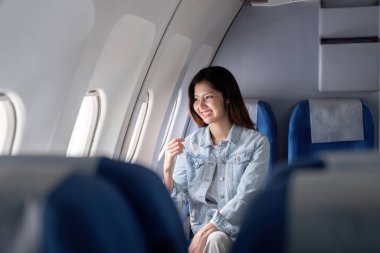 Uçak penceresinin yanında oturan mutlu bir turist, manzaranın ve seyahat deneyiminin tadını çıkarıyor. Seyahat, turizm ve havacılık ile ilgili konular için mükemmel.