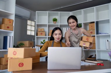 İki arkadaş internet işlerinde birlikte çalışıyor, kutuları paketliyor ve modern bir ofis ortamında dizüstü bilgisayar kullanıyorlar..