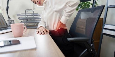 Ofis masasında çalışırken sırt ağrısı çeken bir iş adamı, iş sağlığı ve ergonomik konularını vurguluyor.