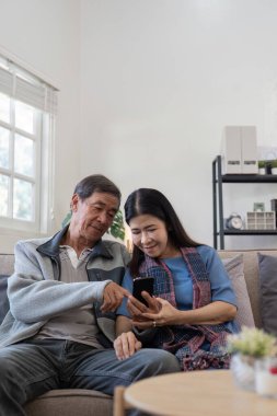 Kanepede oturan yaşlı bir çift alışveriş ve sosyal medya için akıllı telefonu mutlulukla kullanıyor. Günlük yaşamlarında modern teknolojinin neşesini sergiliyorlar..