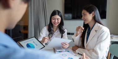 Bir iş ekibi modern bir ofiste veri analizini tartışıyor, tablet ve kağıttaki çizelge ve grafikleri gözden geçiriyor.