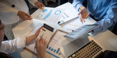 Bir iş ekibi, modern bir ofis ortamında işbirliği içinde, tablolar, grafikler ve raporlar kullanarak finansal analizleri tartışır..