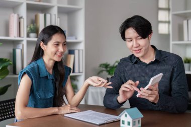 Gayrimenkul alım sözleşmesini tartışan ve imzalayan mutlu bir çift modern ofis ortamında emlak işlemlerini sembolize ediyor..