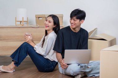 Neşeli bir çift yeni evlerine taşınırken mola veriyor, yerde oturuyor ve etraflarında kutular taşıyor..