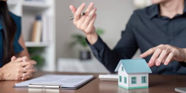 Gayrimenkul alım sözleşmesi imzalayan yakın plan çekimleri. Masanın üzerinde bir model ev ile emlak işlemlerini sembolize ediyor..