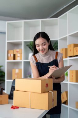 Genç bir kadın çevrimiçi bir ekomünikasyon işinde paket kutuları hazırlıyor ve düzenliyor, modern çevrimiçi satış ve ürün sevkiyatı sürecini gözler önüne seriyor.