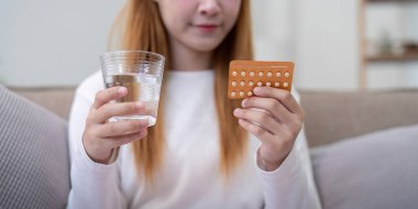 Doğum kontrol hapları ve bir bardak su taşıyan bir kadının, doğum kontrolü, sağlık ve aile planlamasını ön plana çıkardığı yakın plan..