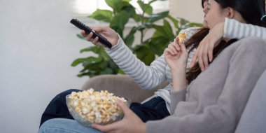Sevgi dolu lezbiyen bir çift rahat bir şekilde koltukta oturur, patlamış mısırlarını paylaşır ve rahat, modern bir oturma odasında birlikte televizyon izlerler..