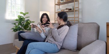 Sevgi dolu bir ilişkisi olan iki kadın şık, modern bir oturma odasında rahat bir kanepede oyun oynayarak eğleniyorlar..