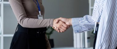 Modern bir ofis ortamında anlaşma ve ortaklığı simgeleyen iki iş adamı el sıkışıyor..
