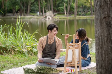 Göl kenarında piknik yapan bir çift, doğayla iç içe sanatsal aktiviteler yapıyorlar..